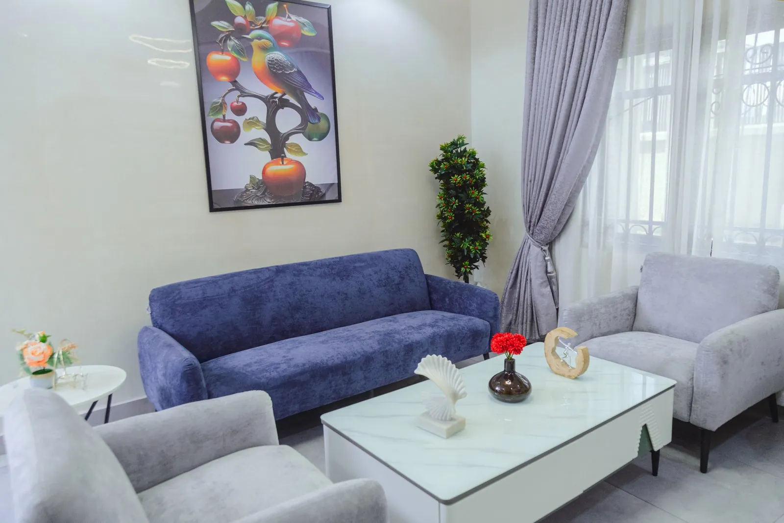 Living room of the Premium Luxury One-Bedroom apartment in Apo, Abuja, with a blue sofa, grey armchairs and a marble coffee table