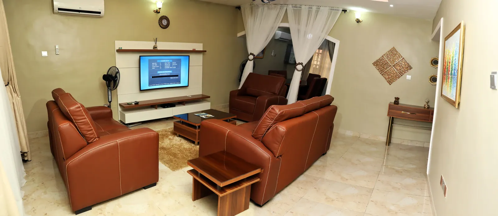 Living room of the Two Bedroom Executive apartment in Lugbe, Abuja, with brown leather sofas and a wall-mounted TV